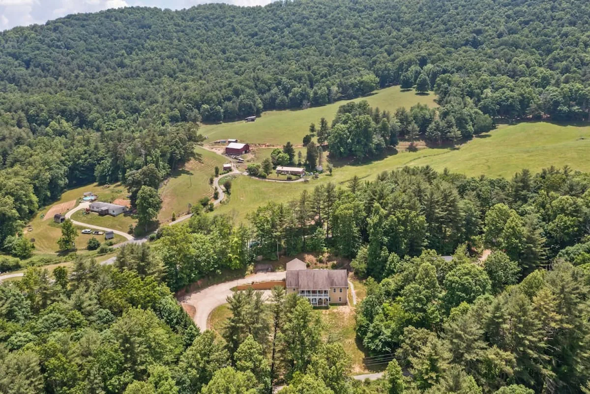 A large house sits nestled among lush greenery, with rolling hills and trees forming a peaceful backdrop. The expansive green landscape and nearby hills emphasize the setting's tranquility and proximity to nature, inviting families to return from outings to a spacious, private retreat.
