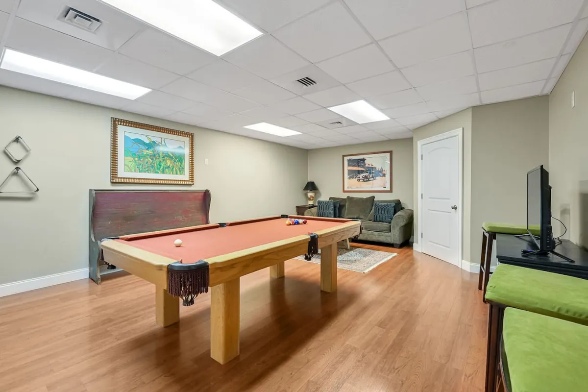 A casual and inviting game room with a pool table, a comfortable sofa, framed artwork, and a television. The space is designed for socializing, playing games, or enjoying movie nights together as a family.