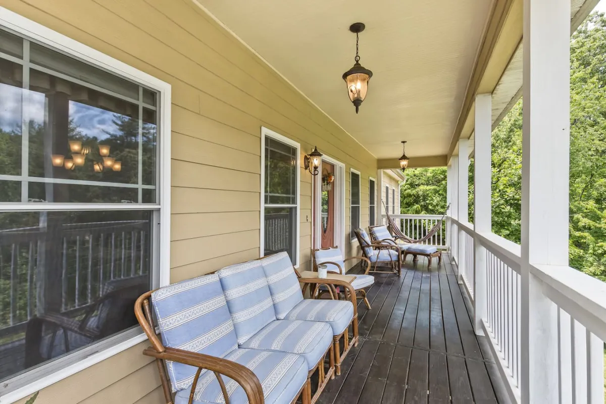 A tranquil exterior setting with comfortable seating, hanging lanterns, and vibrant greenery in the background. The inviting atmosphere is perfect for unwinding with friends, sharing morning coffee, or reminiscing after a day exploring Asheville.