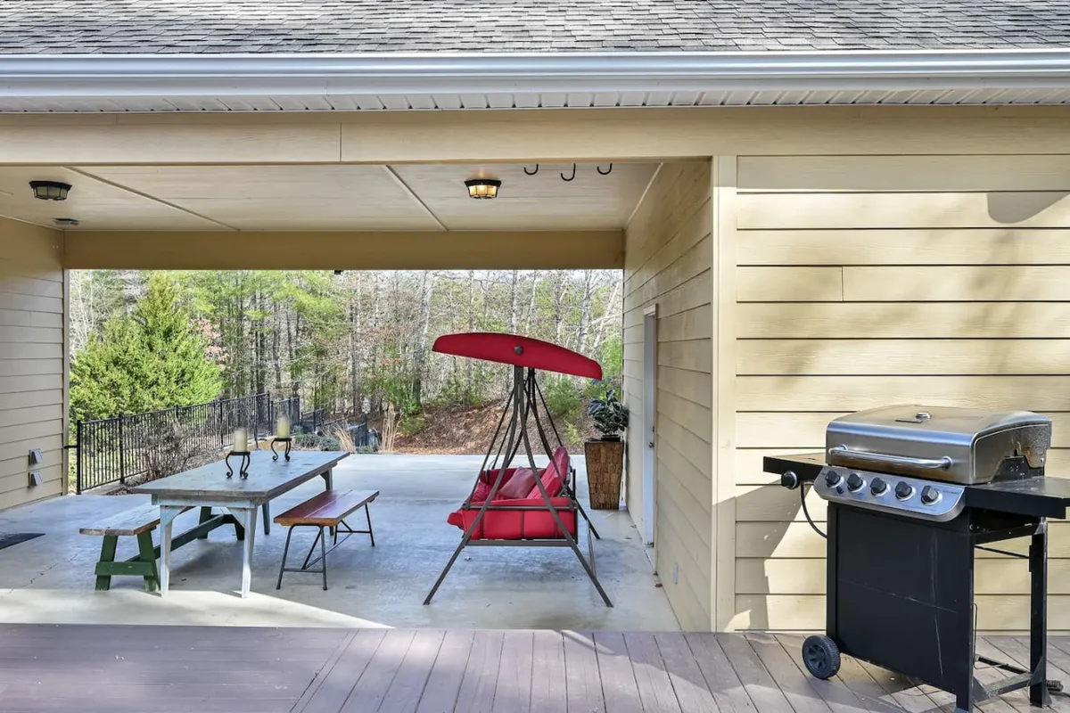 An inviting outdoor area with a red swing seat, a grill, a wooden table, and several outdoor chairs. The setup encourages socializing, dining, and relaxing after a day of exploration. The scene hints at shared meals, grilling sessions, and enjoying mountain sunsets with family or friends.