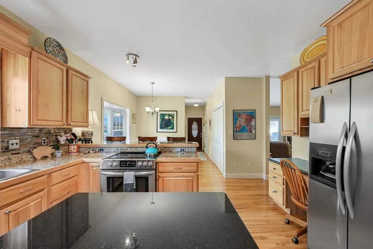 This kitchen features modern stainless steel appliances, a granite countertop, and a welcoming kitchen island. Warm wood cabinets frame the space, creating a functional and inviting cooking area perfect for hosting or casual meals.