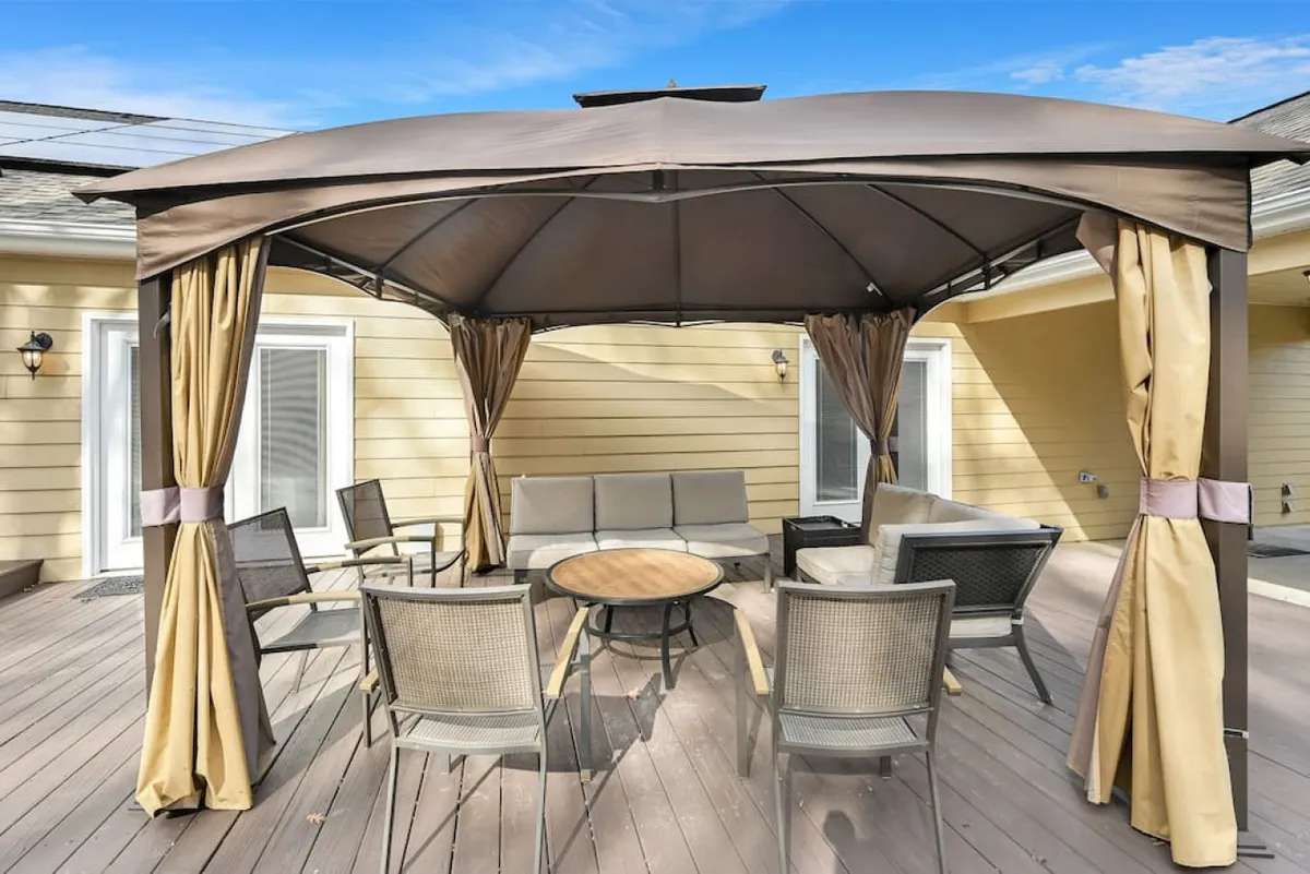 A beautiful gazebo with an elegant seating arrangement and a table sits in a landscaped garden. The setting radiates a casual, welcoming atmosphere, ideal for relaxing, entertaining, or savoring starlit nights and sunset views.