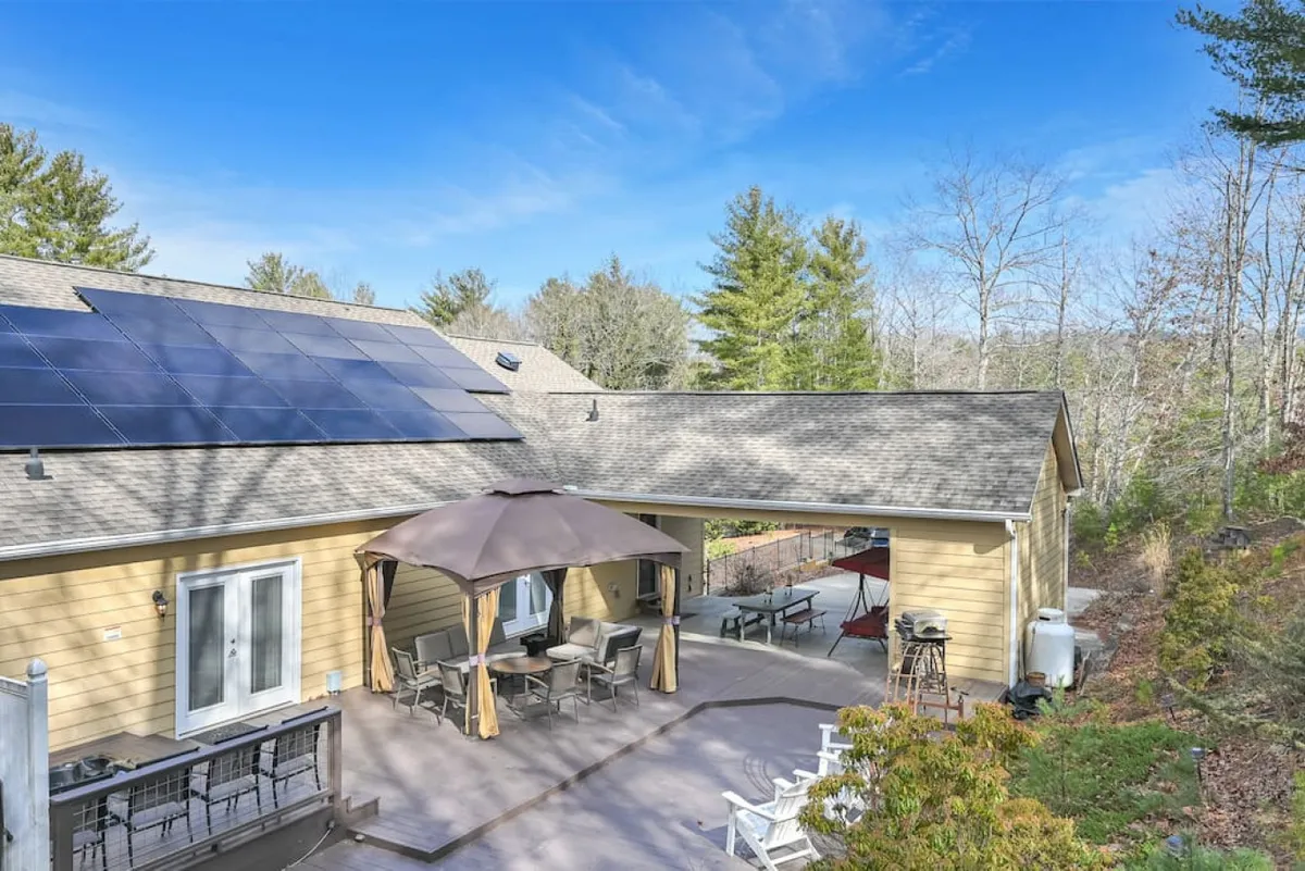 A spacious outdoor patio area is shown, featuring a canopy over comfortable seating. Solar panels are visible on the roof, and the setting highlights the tranquil, natural surroundings. The inviting arrangement is ideal for relaxing, dining, or entertaining guests, with ample space for groups and a scenic view of the surrounding landscape.