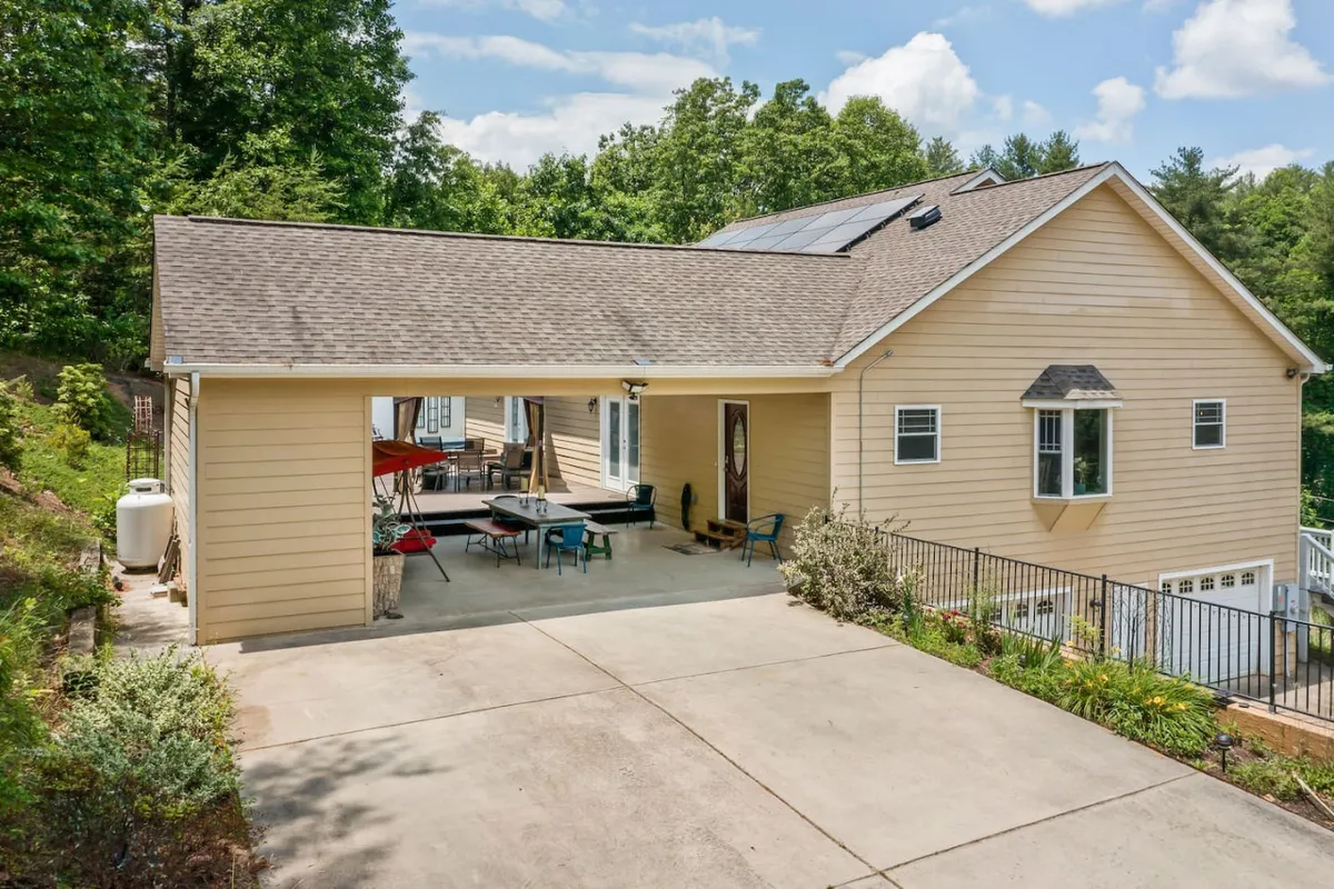 A sunlit exterior view featuring a spacious outdoor seating area, the garage entrance, and landscaped gardens. The patio is inviting and well-suited for gatherings, with ample seating and space for guests to mingle. Solar panels hint at a modern, sustainable touch.